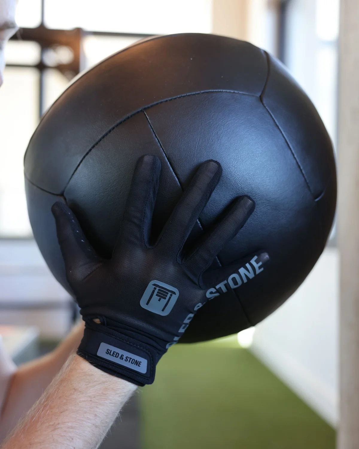 The back of the Sled & Stone glove flat against a med ball, sled mark and wordmark to camera