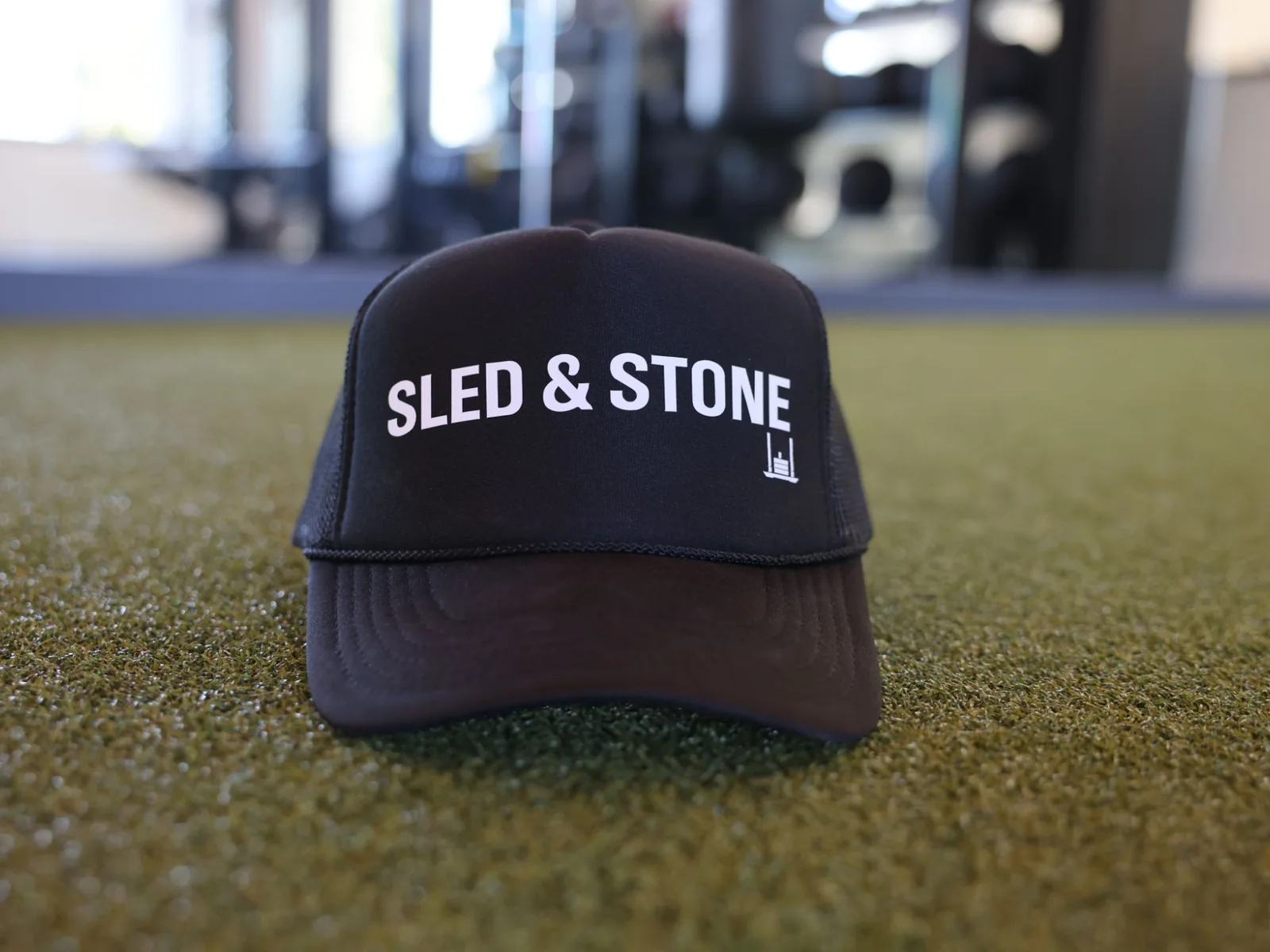 The black Sled & Stone trucker, laid on turf, Sled & Stone printed across the front — view 2