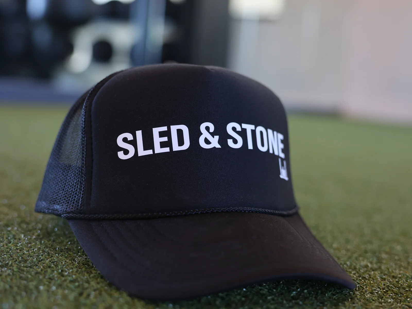 The black Sled & Stone trucker, laid on turf, Sled & Stone printed across the front